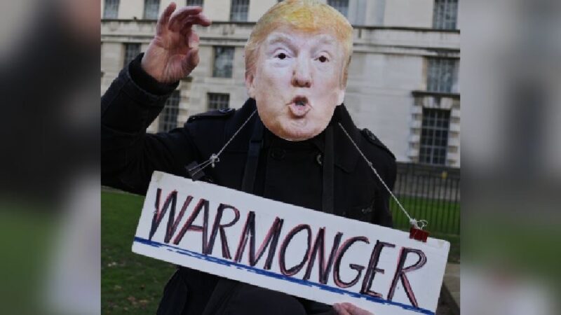 Protester dressed like Trump with sign saying warmonger hanging from their neck
